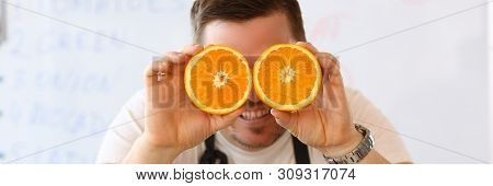 Man Holds Halves Of Cut Orange As Eye Glasses Portrait Background Concept