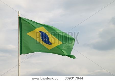 Brazilian Flag On A Blue Sky With Clouds Background