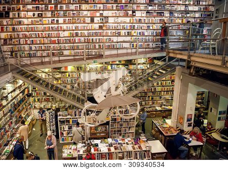 Lisbon, Portugal: Many Old Books And Customers Of The Popular Bookstore Ler Devagar With Artworks An
