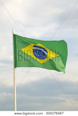 Brazilian Flag On A Blue Sky With Clouds Background