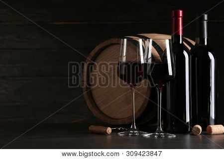 Composition With Glasses And Bottles Of Red Wine On Table Against Dark Background. Space For Text