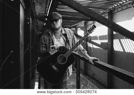 Bluesman with acoustic guitar in grayscale. Cool guy looks into smartphone. Wandering blues musician. Brutal bearded man travels light. Wandering hippie lifestyle. Eccentric man in monochrome.