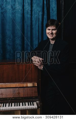 Classical Musician Performer Near Piano. Musical Artist In Dark Room Of Culture House. Portrait Of C