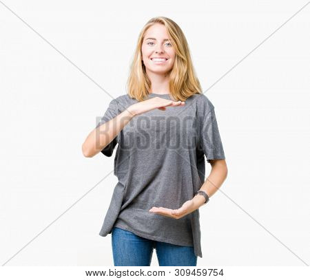 Beautiful young woman wearing oversize casual t-shirt over isolated background gesturing with hands showing big and large size sign, measure symbol. Smiling looking at the camera. Measuring concept.