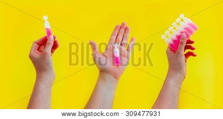 Female Hand Holding Pink Liquid Medicine In An Ampoule, Isolated On Yellow Background.