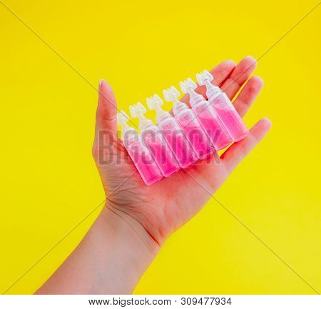 Female Hand Holding Ampoules With Pink Liquid Medicine, Isolated On Yellow Background.