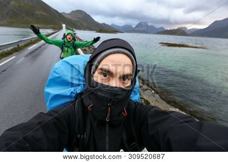 Self Portrait Of Two Young Men Hiking Behind Each Other On A Street On Lofoten Islands In Norway. Th