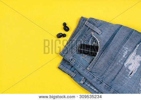Flat Lay Composition With Wireless Earbuds, Jeans And Charging Case In Its Pocket On Yellow Backgrou