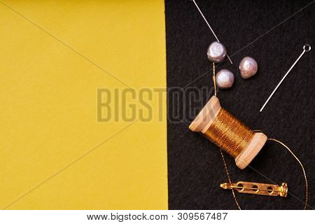 Embroidery Products And Tools. Coil Metal Threads, Pearls And A Pin With The Needle On The Black Fel