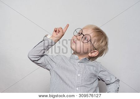 Portrait Of A Cute Blond Boy With Big Glasses. Finger Pointing Up. White Background.