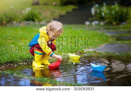 Child With Paper Boat In Puddle. Kids By Rain.