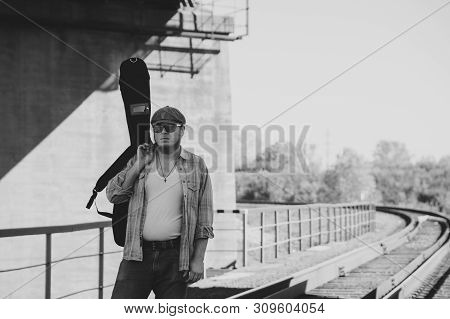 Bluesman With Guitar Case Walks On Railroad. Blues Musician On Railway In Grayscale. Cool Guy With G