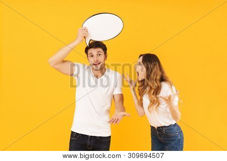 Portrait of angry couple in quarrel man and woman arguing while holding blank thought bubble isolated over yellow background