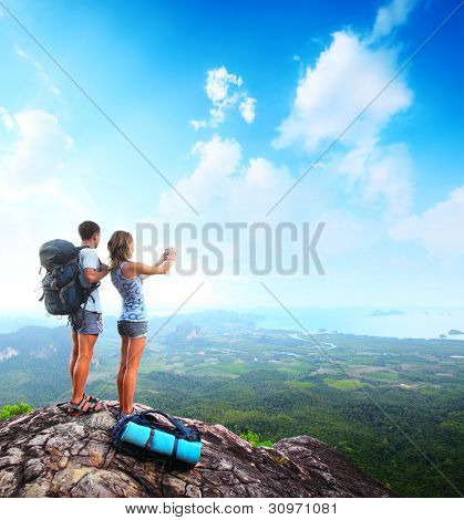 junge Touristen mit Rucksäcken unter Foto des Tales von Spitze eines Berges