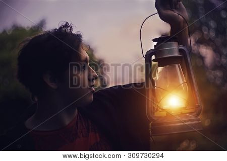 The Guy Stands At Night In A Dark Scary Forest With An Old Lighted Kerosene Lamp In His Hand And Loo