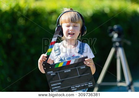 Portrait Of A Child With A Tv Clapper. Television Numerator. A Little Girl In Headphones With A Tv N