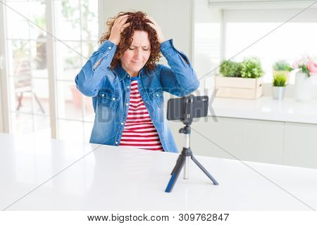 Senior woman doing video chat using smartphone camera suffering from headache desperate and stressed because pain and migraine. Hands on head.