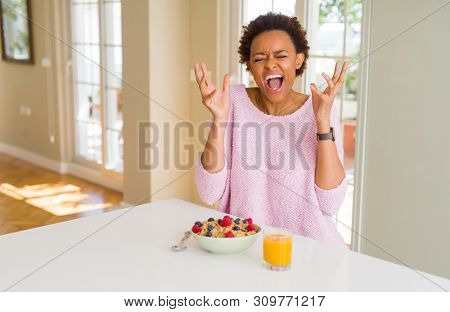 Young african american woman having healthy breakfast in the morning at home celebrating mad and crazy for success with arms raised and closed eyes screaming excited. Winner concept
