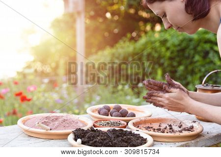Woman Is Manufacturing Seed Balls Or Seed Bombs On A Wooden Table, Flower Field In The Background