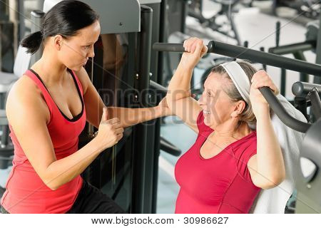 Entrenador personal ayudar a senior mujer haciendo ejercicio en la máquina en el gimnasio