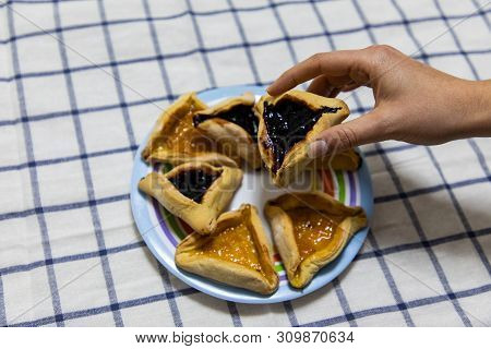 Woman Hand Holding Hamantash Purim Blueberry And Apricot Jam Cookies On Colored Plate On Blue And Wh