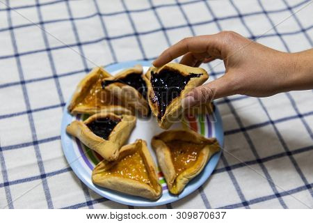 Woman Hand Holding Hamantash Purim Blueberry And Apricot Jam Cookies On Colored Plate On Blue And Wh