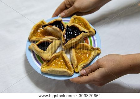Woman Hands Holding A Colored Plate With Hamantash Purim Blueberry And Apricot Jam Cookies On White