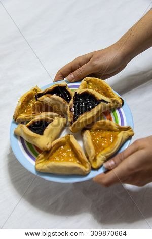 Woman Hands Holding A Colored Plate With Hamantash Purim Blueberry And Apricot Jam Cookies On White