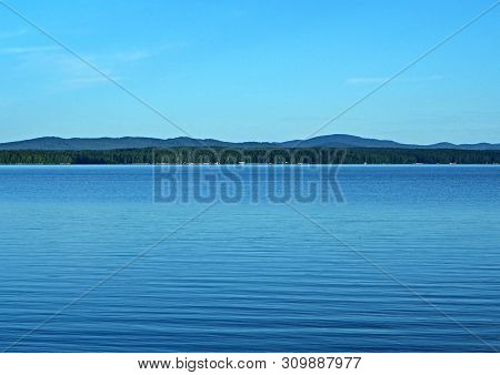 View Of The Opposite Shore Of The Calm Morning Lake, The Blue Sky Reflected In The Water, Southern U