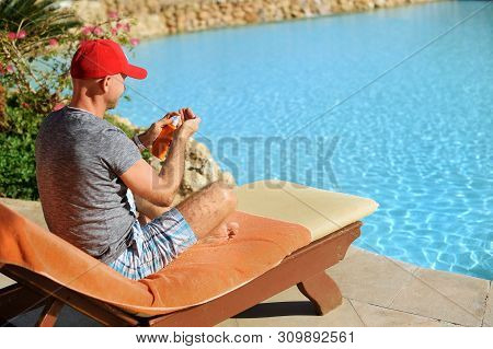 Young And Successful Man On A Sun Lounger Squeezes Out Sunblock Cream From A Tube At The Hotel Near 