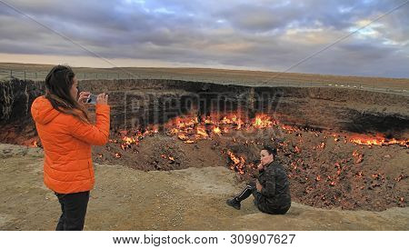 Turkmenistan, Darvaza - March 21, 2019: Girls Make A Photo On The Background Of The Burning Crater 