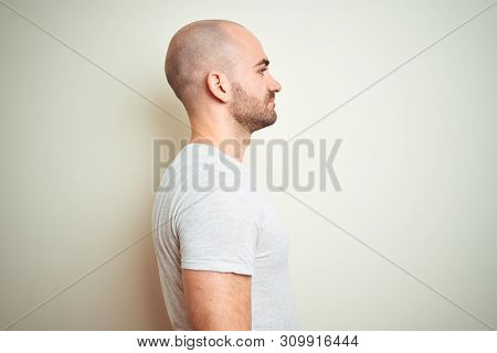 Young bald man with beard wearing casual white t-shirt over isolated background looking to side, relax profile pose with natural face with confident smile.