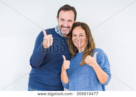 Beautiful middle age couple in love over isolated background success sign doing positive gesture with hand, thumbs up smiling and happy. Looking at the camera with cheerful expression, winner gesture.