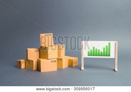 Plenty Of Cardboard Boxes And Whiteboard With Green Positive Trend Chart. Rate Growth Of Production 