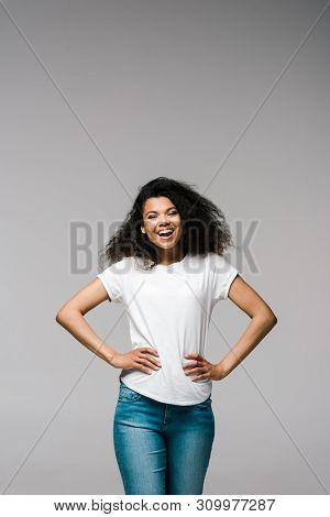 Happy Young African American Woman Smiling While Standing With Hands On Hips On Grey