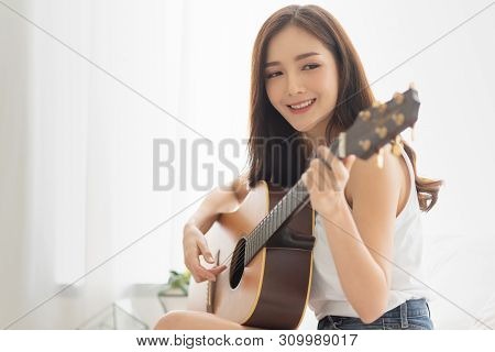 Pretty Asian Woman Is Practicing Guitar With Copy Space. Relaxing Girl With The Instrument In The Wh