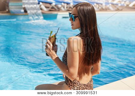 Back View Of Young Pretty Woman Drinking Cocktail Against Outdoor Pool. Female With Perfect Tanned S