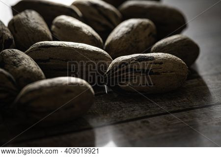 A Macro Shot With Selective Focus Of A Handful Of Pecan Nuts In Shells Set On A Wood Table.