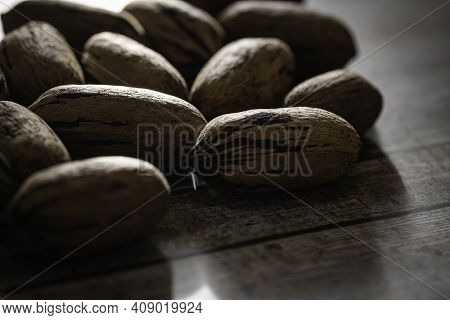 A Macro Shot With Selective Focus Of A Handful Of Pecan Nuts In Shells Set On A Wood Table.