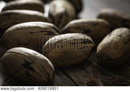 A Macro Shot With Selective Focus Of A Handful Of Pecan Nuts In Shells Set On A Wood Table.