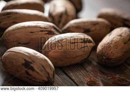 A Macro Shot With Selective Focus Of A Handful Of Pecan Nuts In Shells Set On A Wood Table.