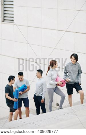 Group Of Cheerful Young People With Yoga Mats Walking Up The Strairs And Discussing Morning Class Th