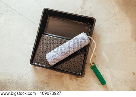 The Paint Cuvette And Roller Lie On The Concrete Floor
