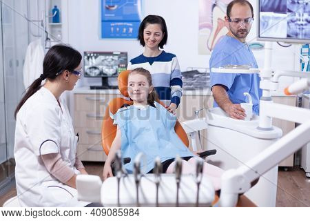 Happy Little Girl At Pediatric Dentist Wearing Dental Bib During Stomatology Examination. Child With