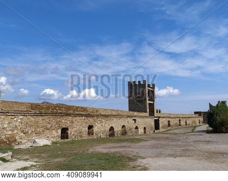 Part Of The Fortress Wall In The City Of Sudak In The Crimea Against The Blue Sky In Summer. Travel