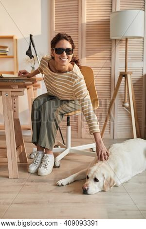 Vertical Full Length Portrait Of Modern Blind Woman Sitting At Table In Cozy Home Interior And Petti