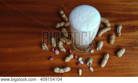 Tall Glass Filled With Cold Tasty Beer With A Frothy Head And Peanuts In Shell Scattered On The Tabl