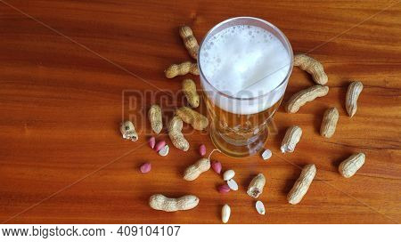 Tall Glass Filled With Cold Tasty Beer With A Frothy Head And Peanuts In Shell Scattered On The Tabl