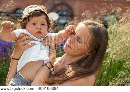 Portrait Of A Young Beautiful Mother With A Moody And Naughty Little Child Baby Boy In Her Arms On A