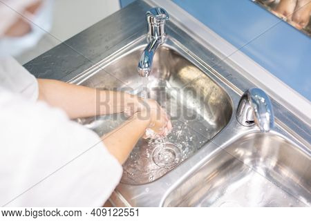 Young assistant, nurse or doctor in white uniform washing hands over one of two metallic sinks before or after medical procedure in clinics